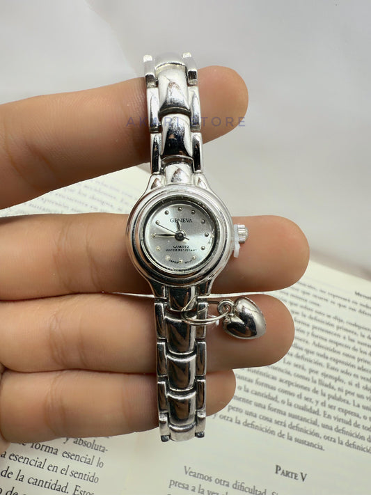 Reloj plateado circular con dije de corazón